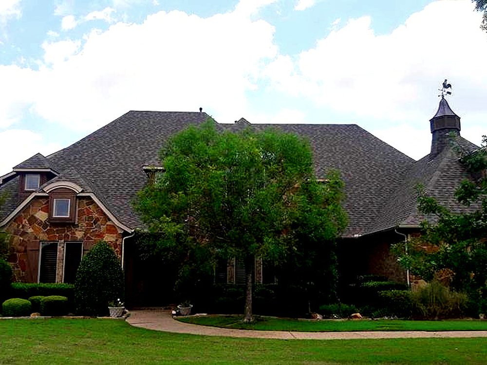 Front elevation of a large stone home with a steep multi-gable roof and manicured lawn