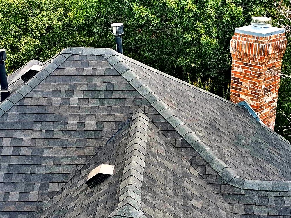 Close view of a shingle roof's hip and ridge lines meeting at a brick chimney