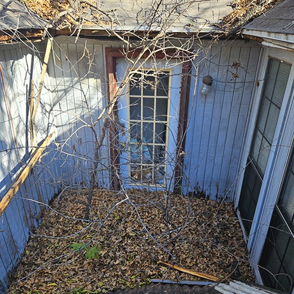 Before: weathered siding and a doorway buried in storm debris